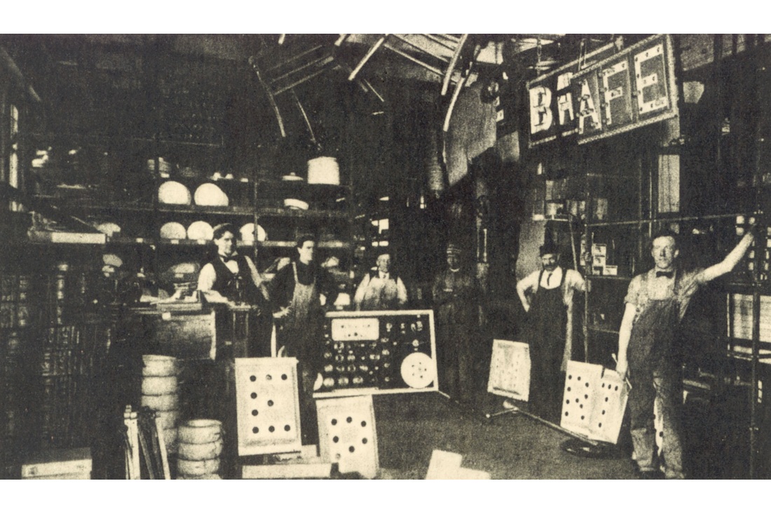 Employees among electric sign parts and equipment in the Federal Electric stockroom and wiring department, circa 1909.