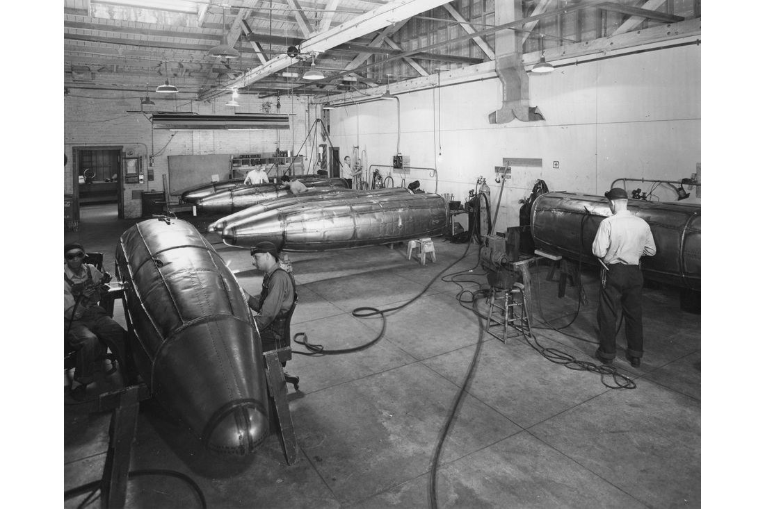 Workers and large metal assemblies on the factory floor during Federal’s World War II production.