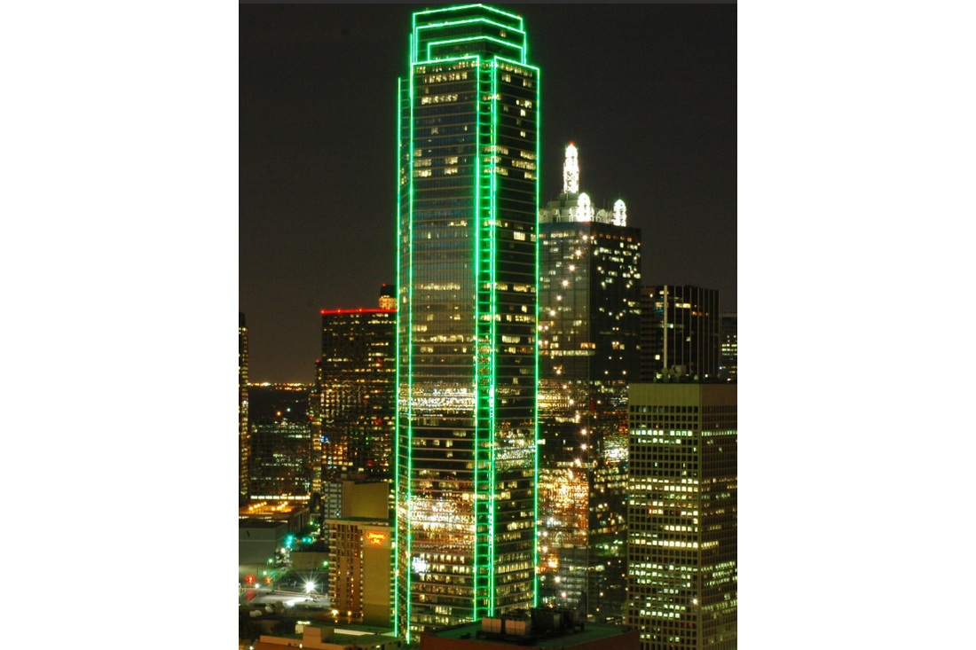 Bank of America Plaza outlined in green light above the Dallas skyline at night.