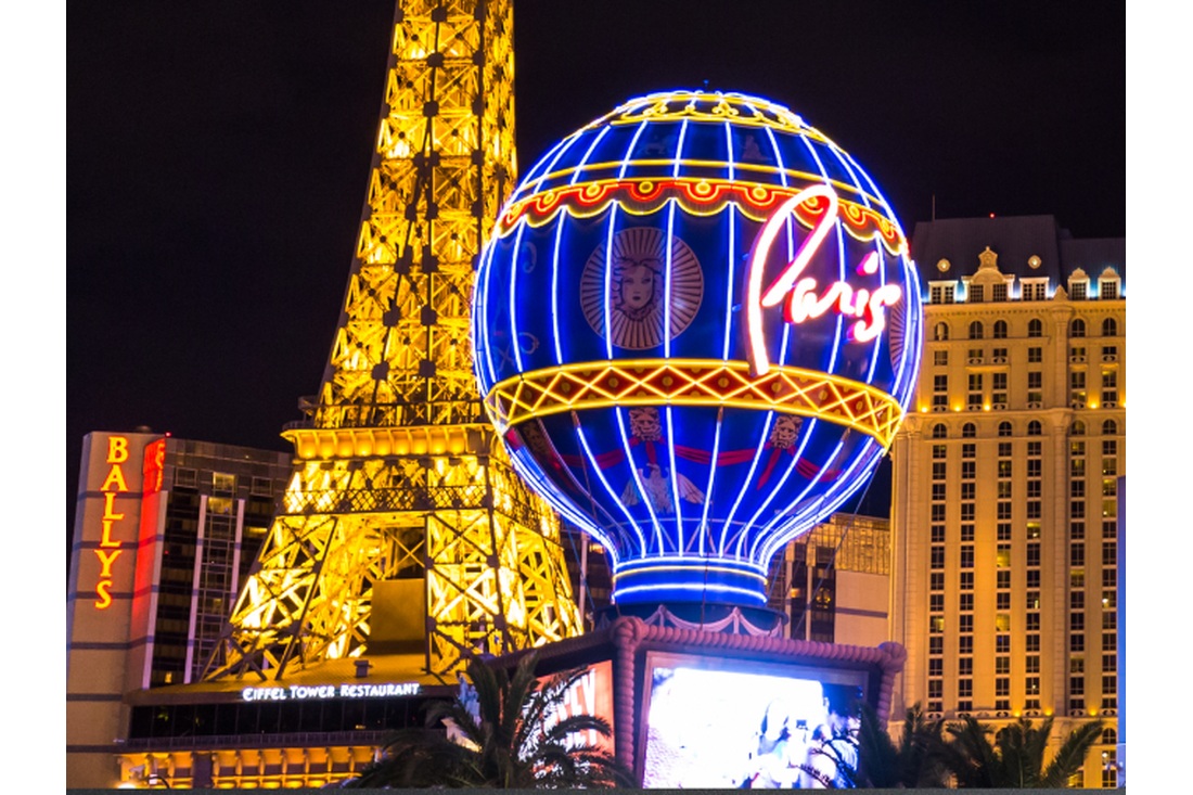 Blue and gold Paris Las Vegas balloon sign illuminated beside the Eiffel Tower replica at night.