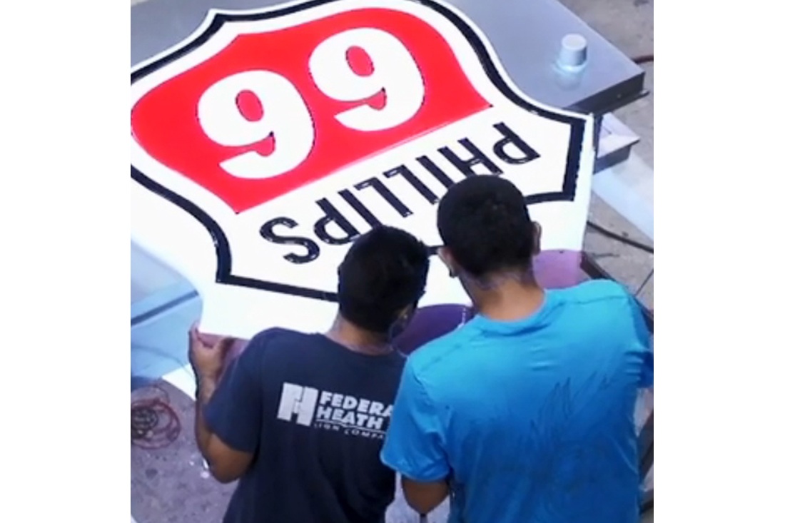 Two employees working on a large Phillips 66 sign in a manufacturing facility.