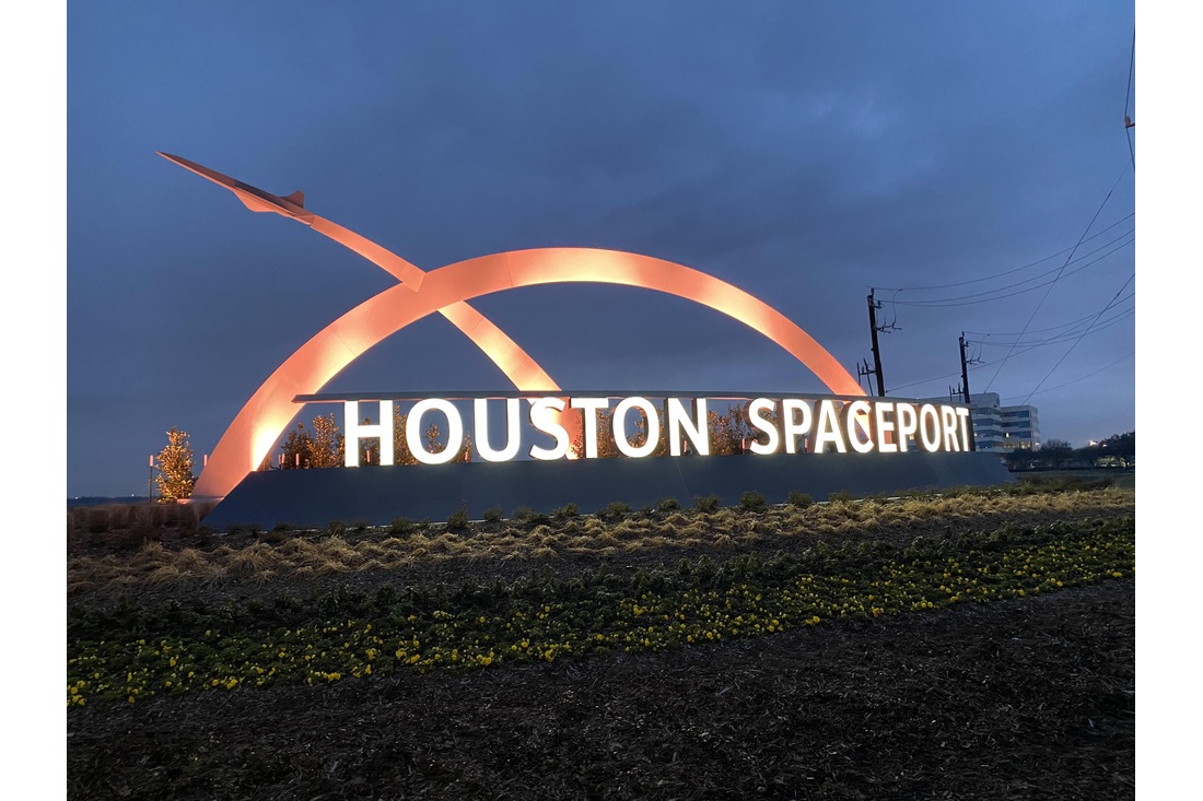 Illuminated Houston Spaceport entrance sign with an orange arch and aircraft silhouette at dusk.