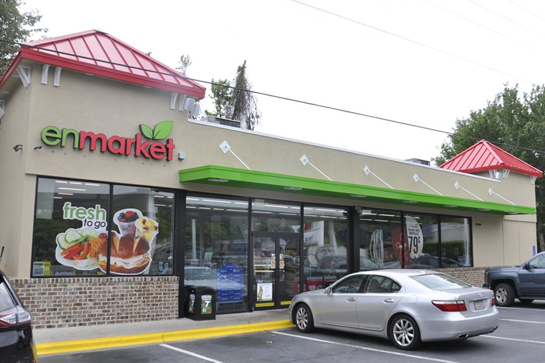Enmarket convenience store exterior with green and red logo signage, green fascia accents, and promotional window graphics.