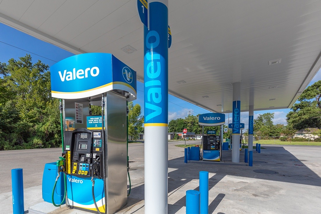 “Valero gas station canopy with a dimensional logo and matching roadside fuel price sign against a blue sky.”