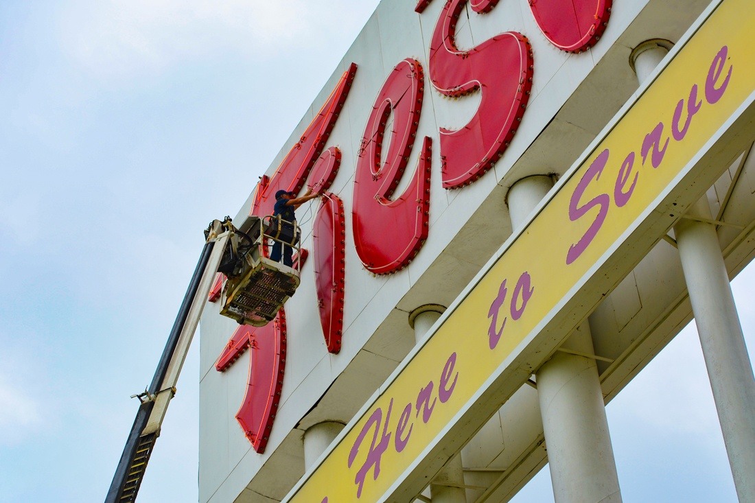 Installer in an aerial lift working on large red exterior grocery store lettering.