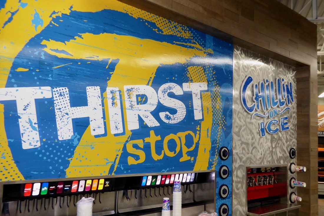 Convenience store beverage station with blue and yellow “Thirst Stop” fountain drink graphics and “Chillin’ on Ice” branding above an ice dispenser.