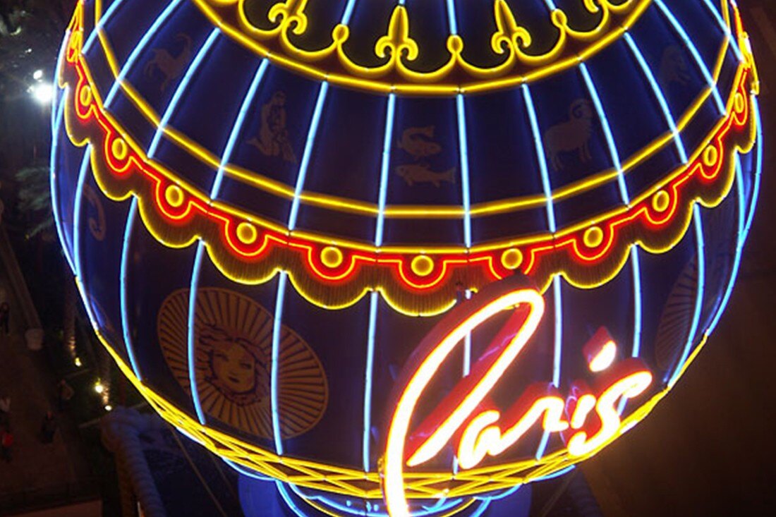 Illuminated Paris Las Vegas balloon sign at night with blue and gold lighting and red script lettering.