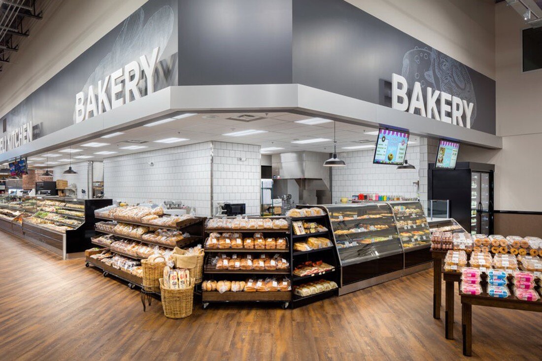 Grocery store bakery department with large overhead “Bakery” lettering, digital menu displays, and bread and pastry cases.
