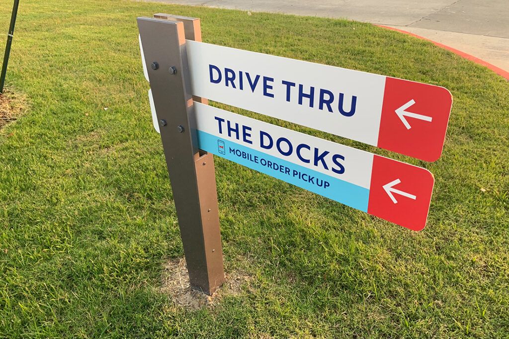 Restaurant directional sign with left-pointing arrows for the drive-thru and The Docks mobile order pickup area.