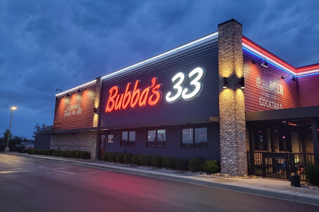 Bubba’s 33 restaurant exterior at dusk with illuminated red and white building signage and red and blue roofline lighting.