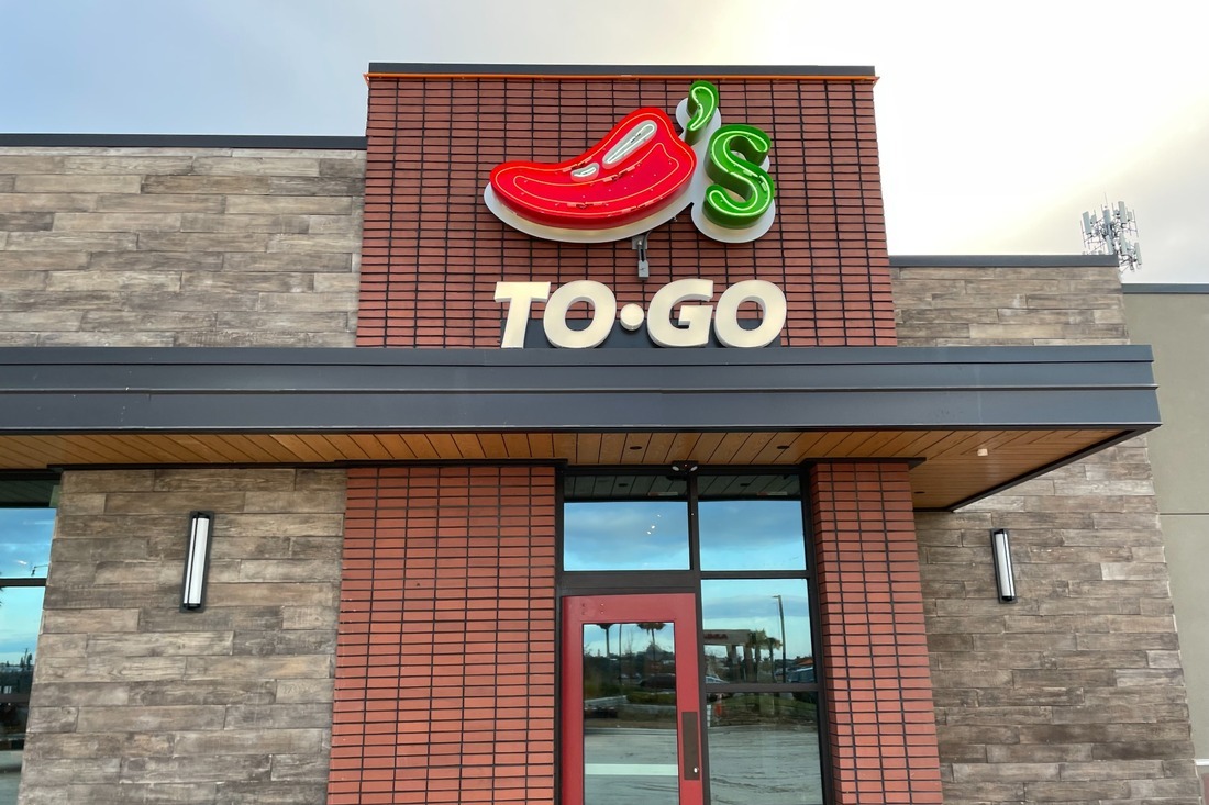 Chili’s To Go entrance with a red chili pepper logo, green lettering, and dimensional To Go signage above a glass door.