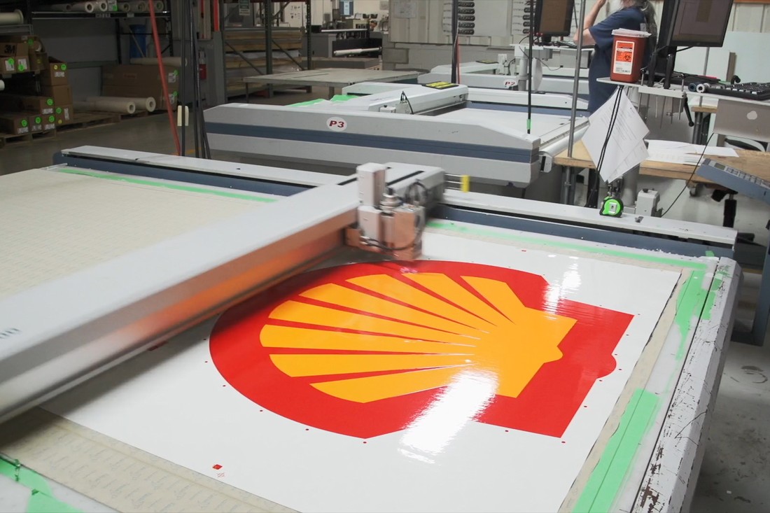 Federal Heath team members inspect a printed Shell logo graphic in a sign manufacturing facility.