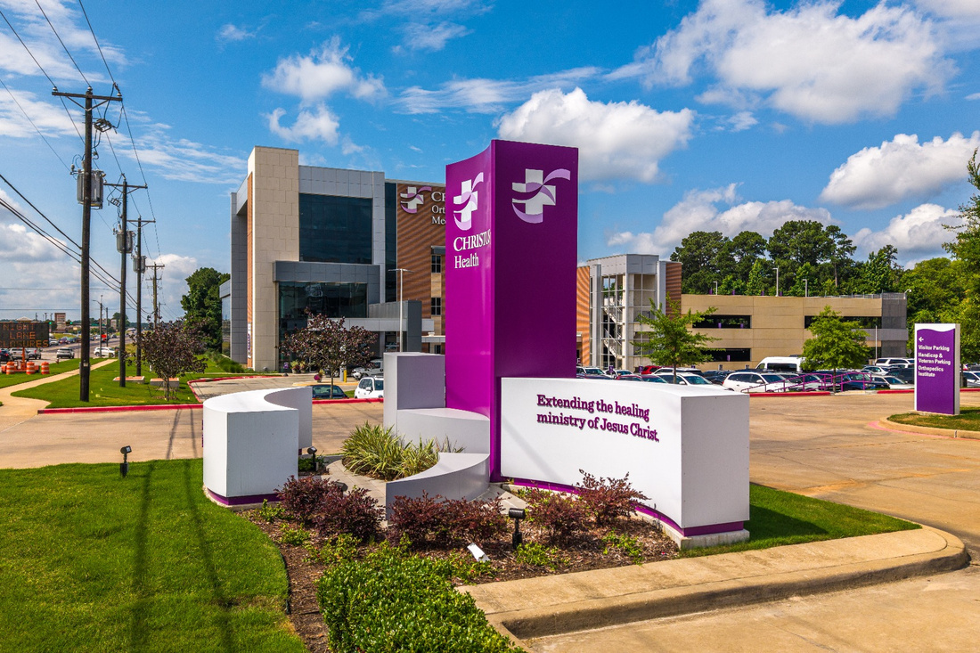 Purple CHRISTUS Health monument sign with curved white architectural elements at a hospital entrance.
