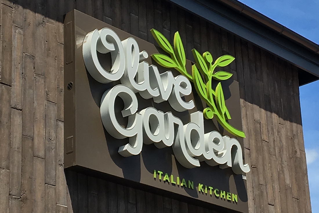 “Olive Garden dimensional lettering and olive branch logo mounted on a stone restaurant facade.”