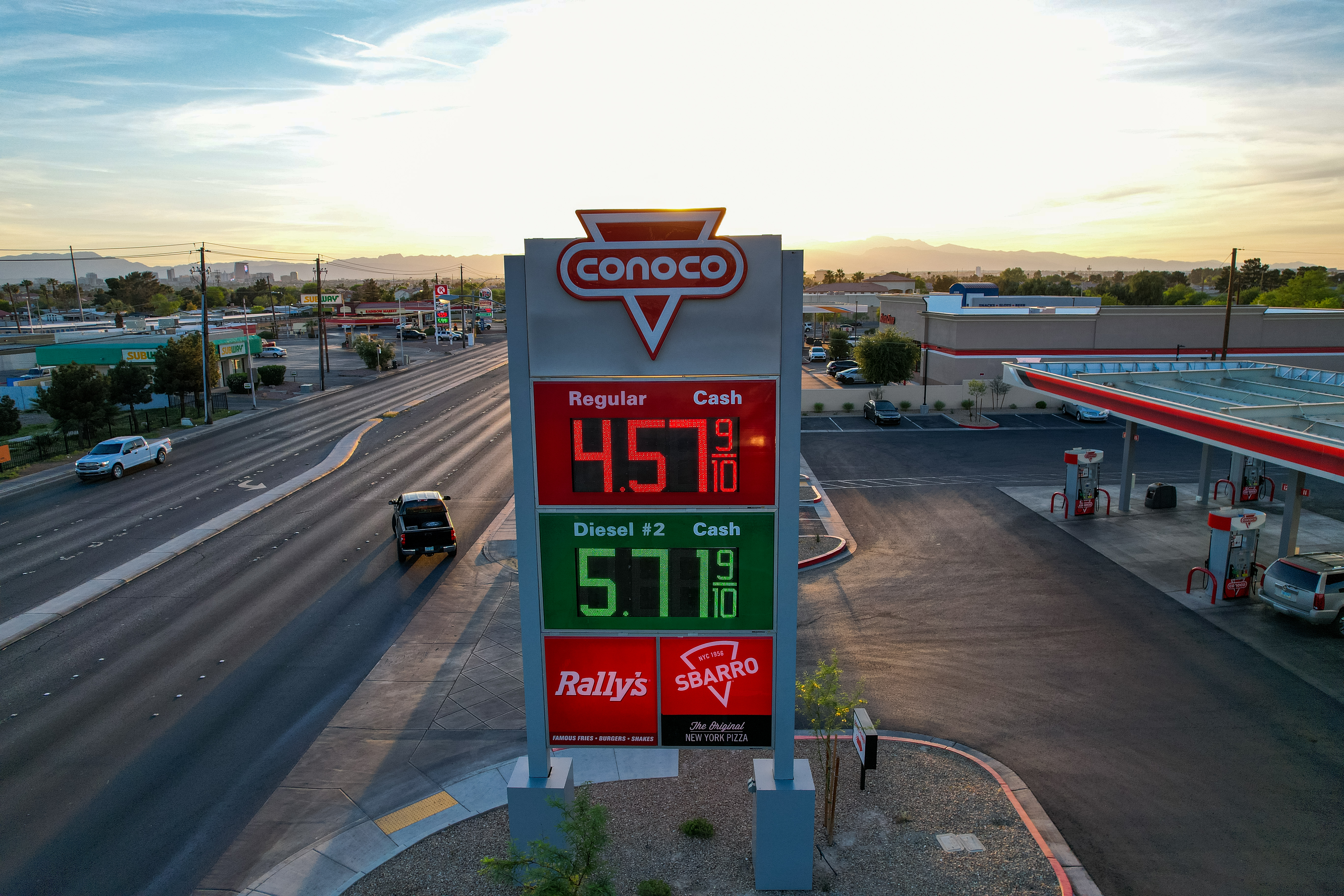 Conoco roadside pylon sign with red and green digital fuel price displays and Rally’s and Sbarro branding at sunset.