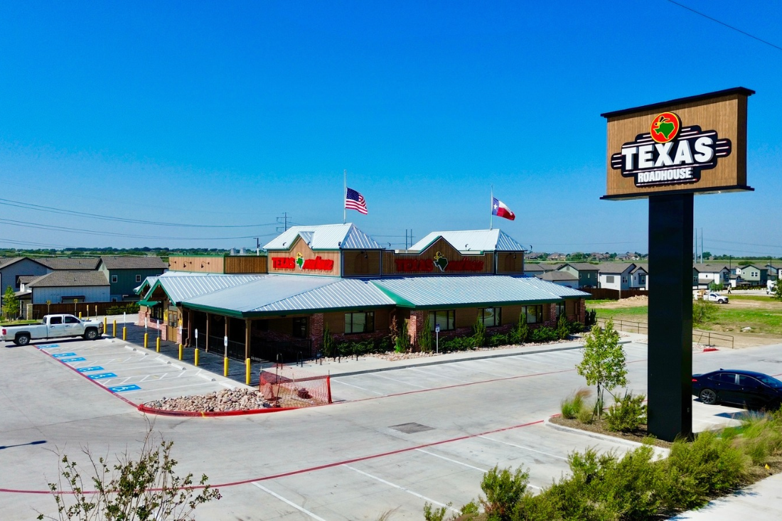 Texas Roadhouse restaurant exterior with branded building signs and a tall roadside pylon sign beside the parking lot.