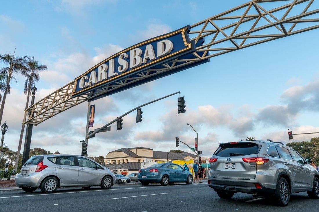 Carlsbad archway sign spanning a palm-lined street above traffic at an intersection.