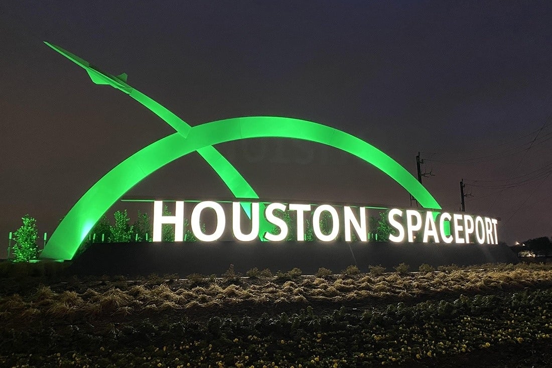 Illuminated Houston Spaceport entrance sign with a green arch and aircraft silhouette at night.