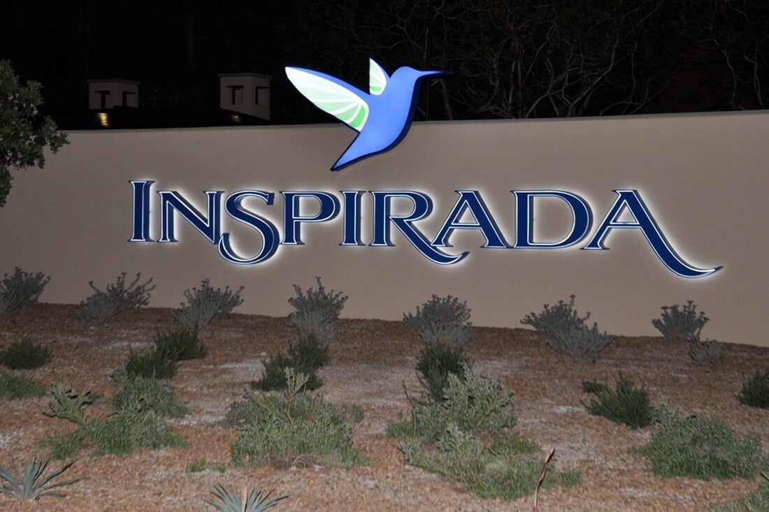 Illuminated Inspirada monument sign with blue lettering and a colorful hummingbird logo at night.
