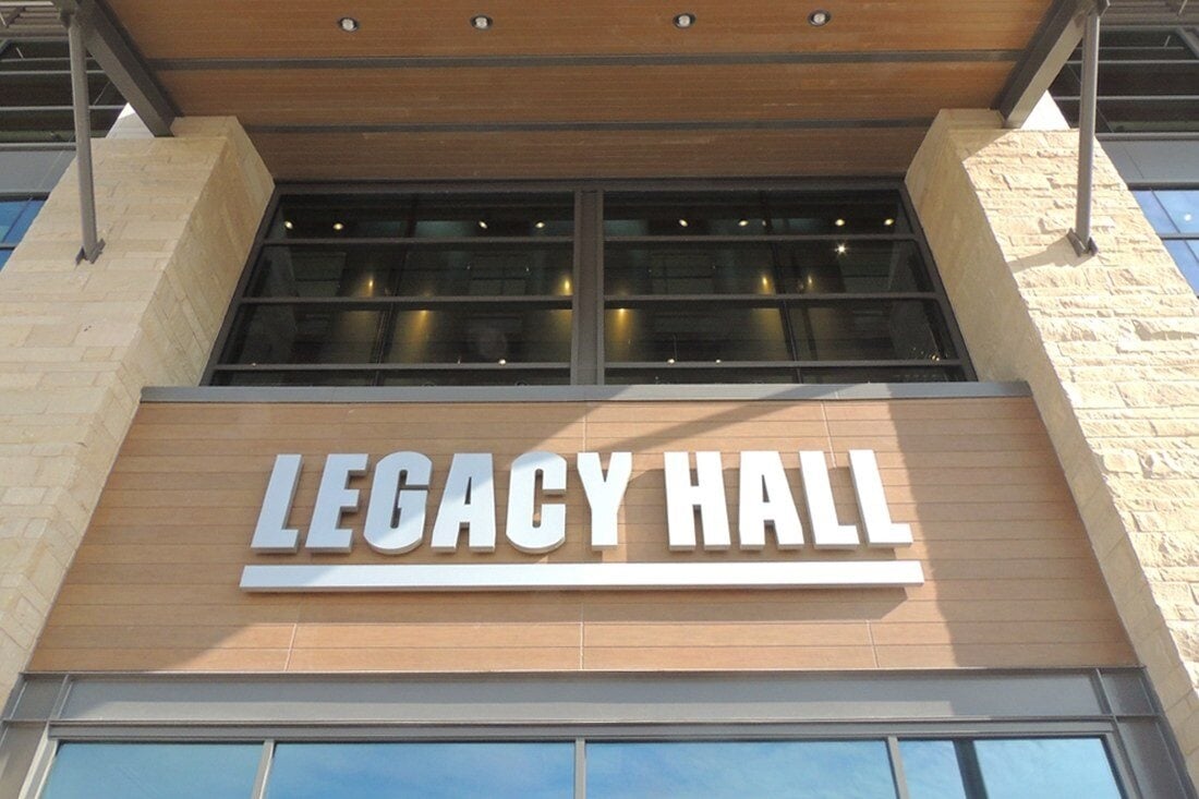 White dimensional Legacy Hall letters mounted above an entrance on a wood-paneled facade.