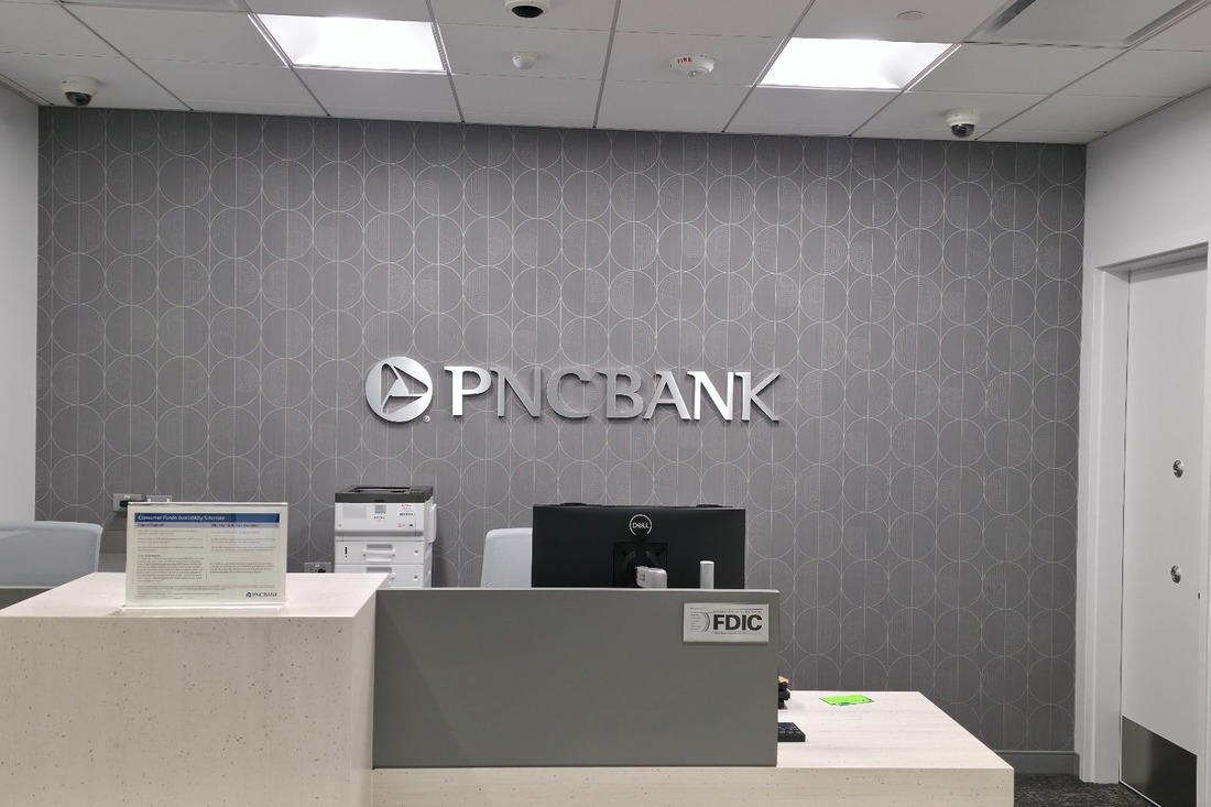 Dimensional PNC Bank lettering and logo on a patterned gray wall behind a branch service counter.