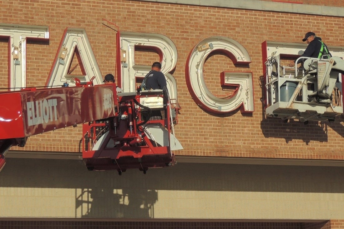 Technicians in bucket lifts servicing large Target letters on a brick store facade.
