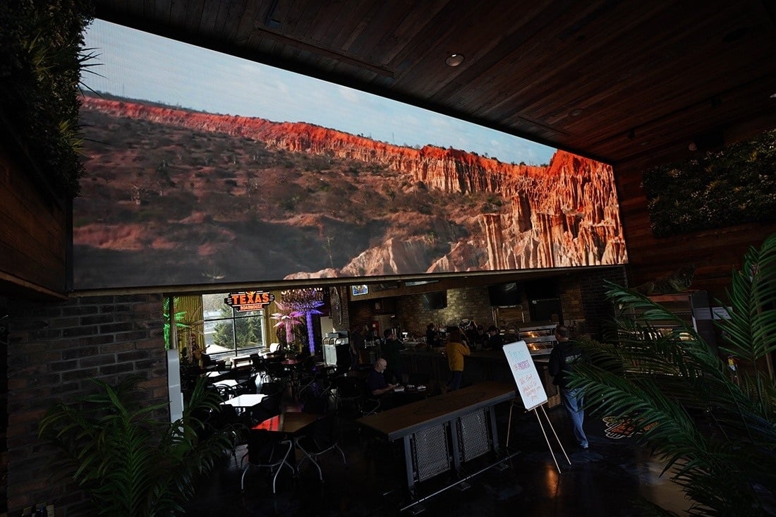 Wide digital display showing a canyon landscape above an interior gathering area at Texas Roadhouse headquarters.
