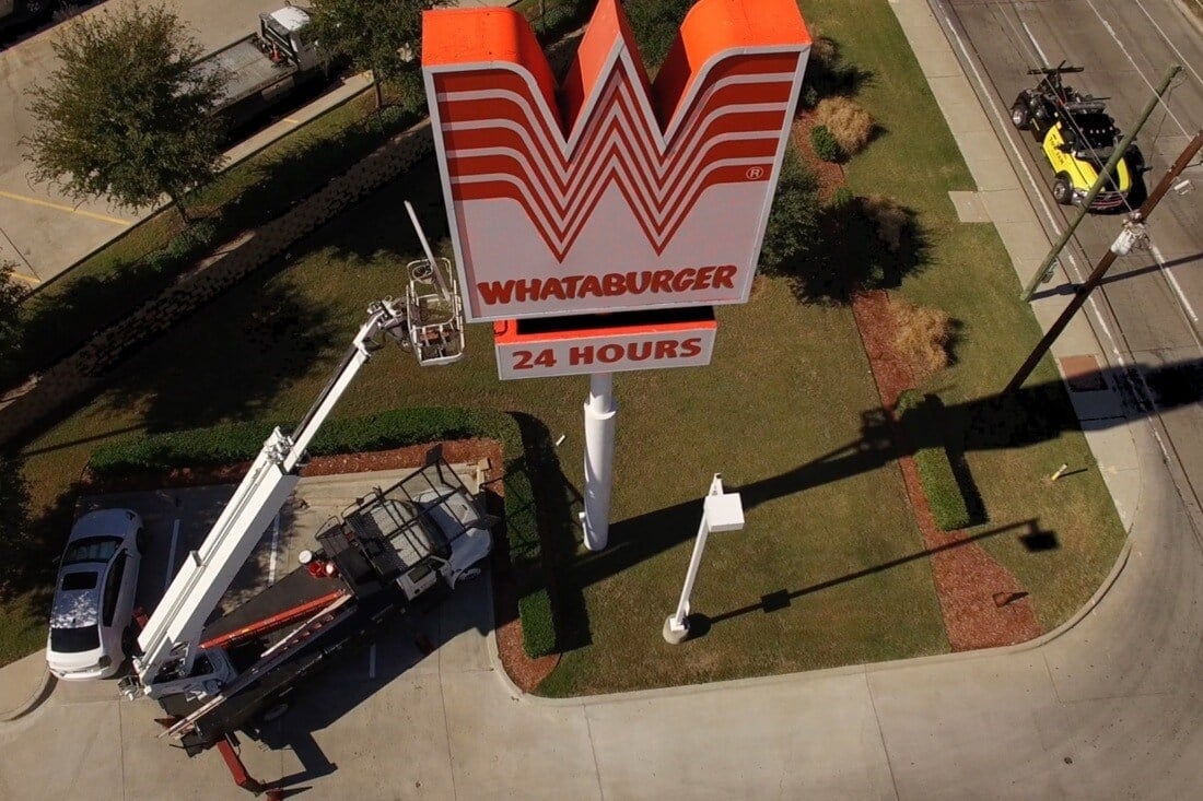 Overhead view of crews in aerial lifts working on a Whataburger pole sign with a 24 Hours panel.