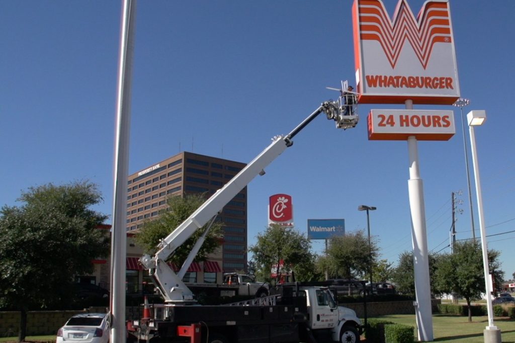 man doing maintenance on whataburger pylon sign